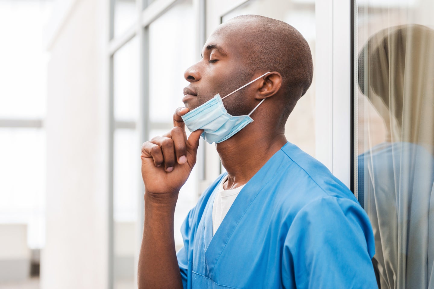 A surgeon in scrubs pulling a mask off their face