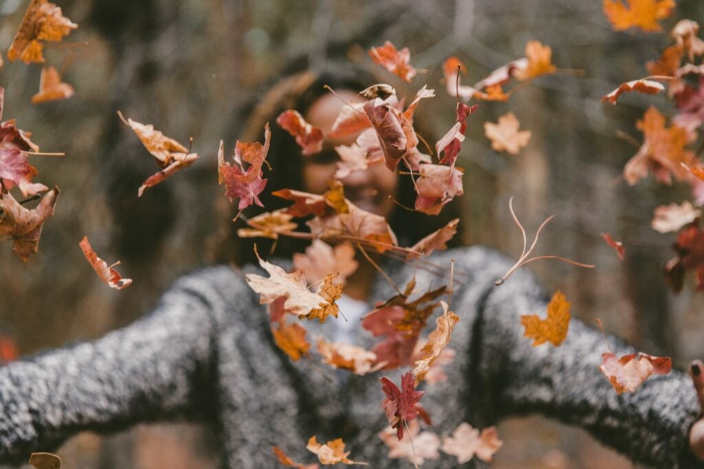 a woman throws fall leaves into the air while smiling