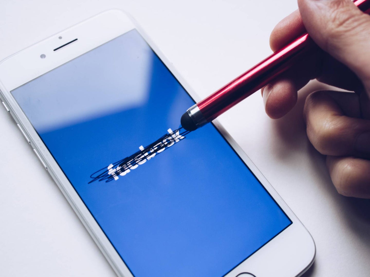 A person using a stylus to cross out the Facebook logo on an iPhone screen.