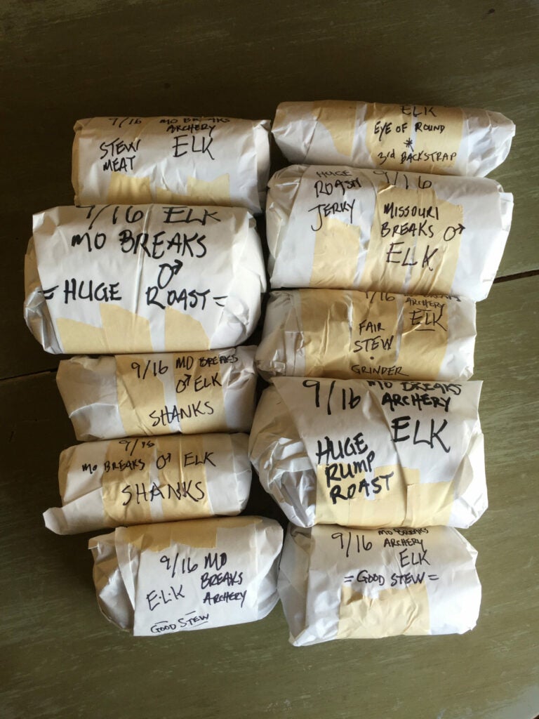 Wrapped packages of elk venison on a table, wrapped in butcher paper and venison with writing on them.