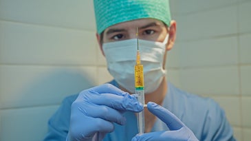 A man in medical PPE holds a syringe full of yellow liquid