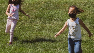 Two kids running on a lawn with masks on