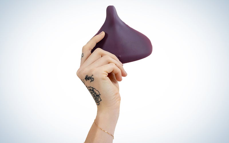 Una mano sostiene una pieza de plástico violeta con forma de asiento de bicicleta.