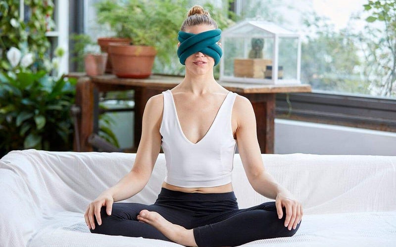 a woman sits cross legged with a blue mask wrapped around her head