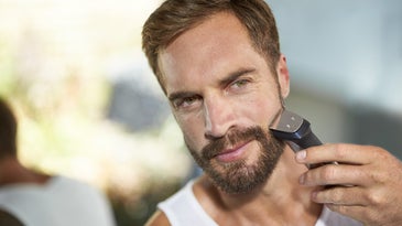 Man with a beard using an electric shaver.