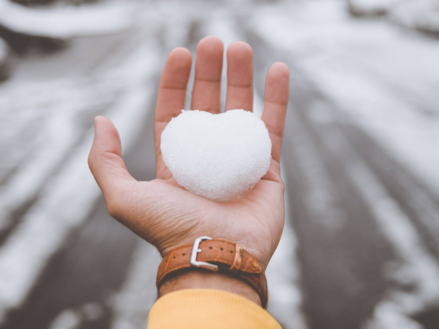 Bare hand holding heart-shaped snow ball.