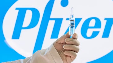 A Uzbekistani doctor holds up a dose of the Pfizer COVID-19 vaccine in front of the company's logo.