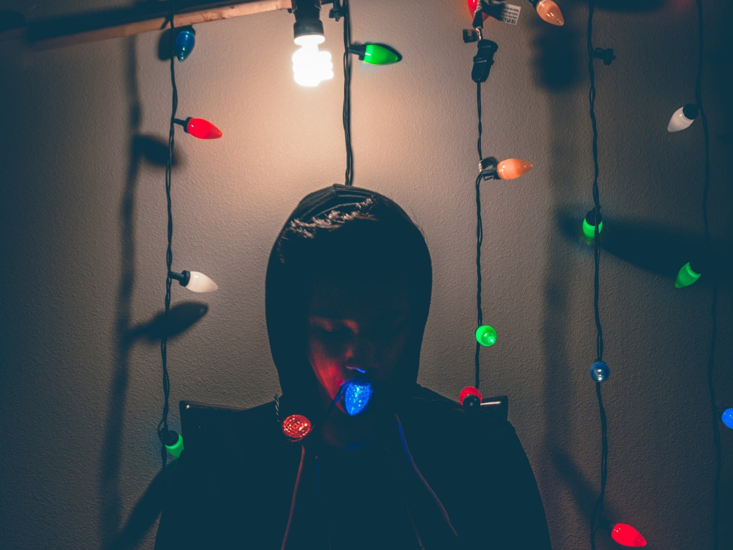 Person sitting under a light in a dark room to store holiday decorations, surrounded by Christmas lights