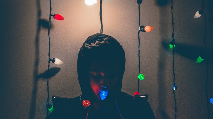 Person sitting under a light in a dark room to store holiday decorations, surrounded by Christmas lights