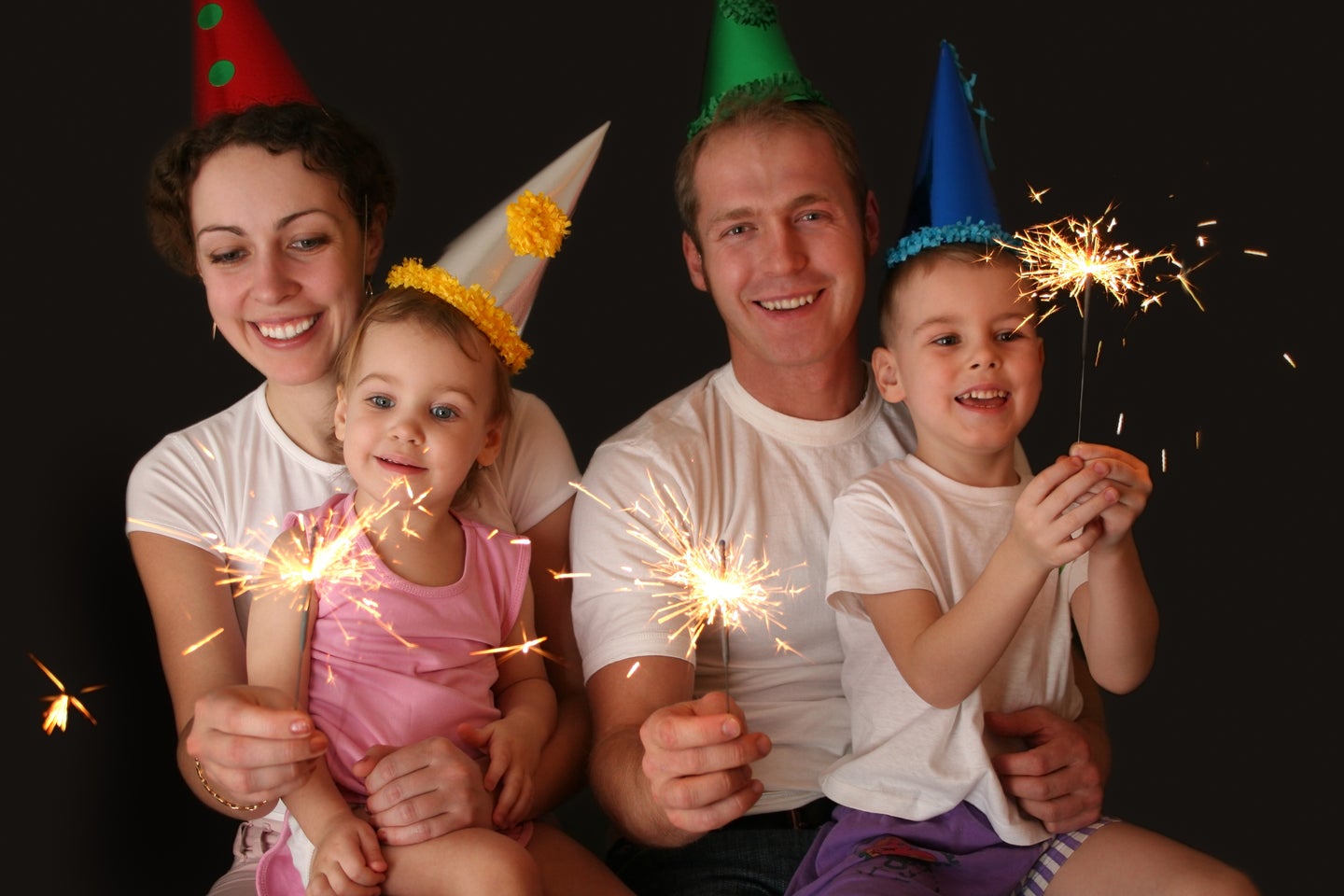 Parents and two kids on New Year's in party hats and sparklers