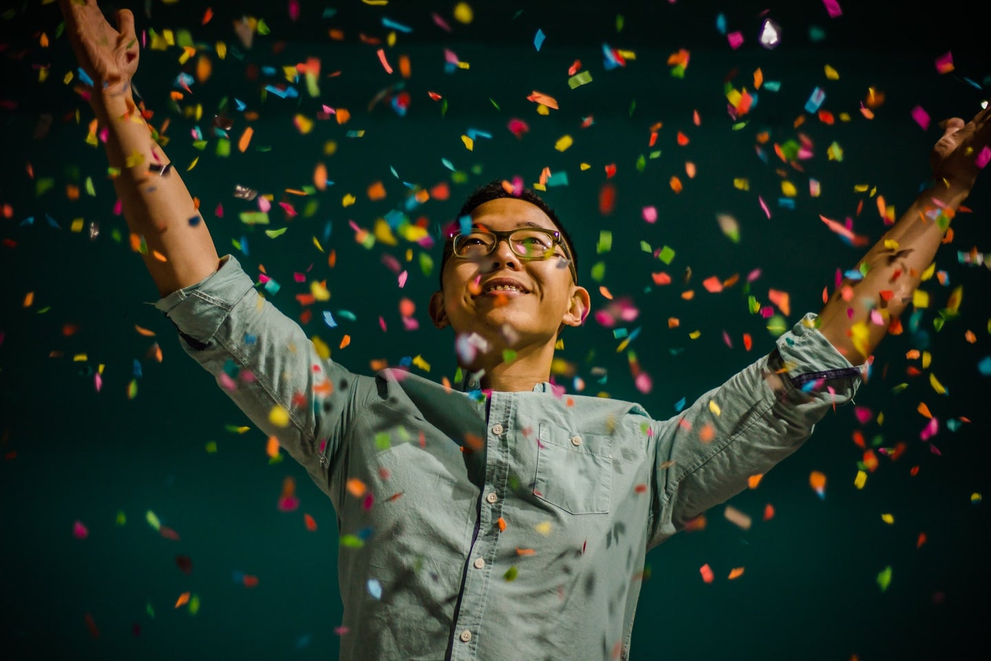 A person in glasses and a buttoned shirt tossing a handful of colorful confetti in the air