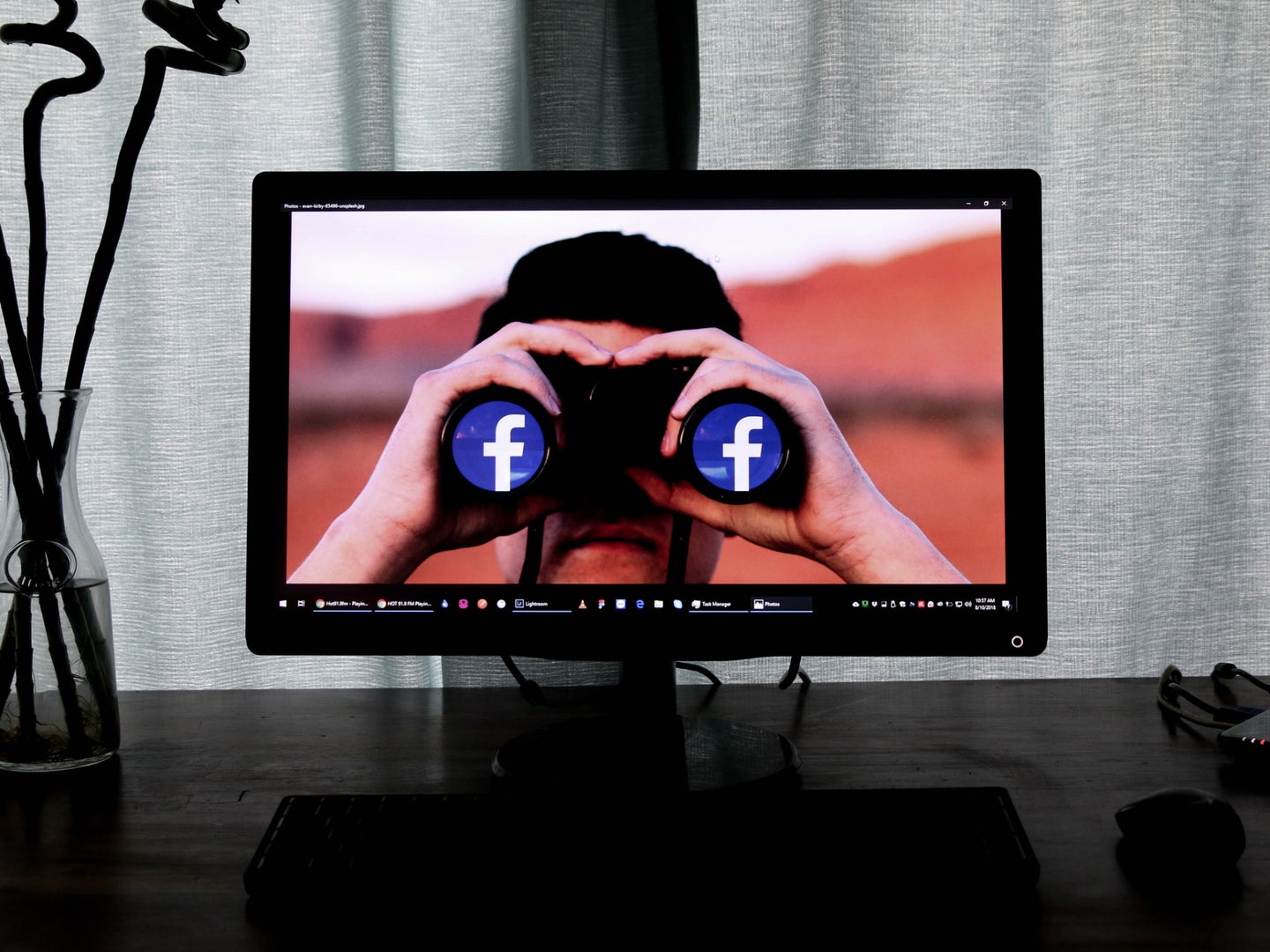 A man use binoculars with the Facebook icon on the lenses looking out from a desktop computer screen.