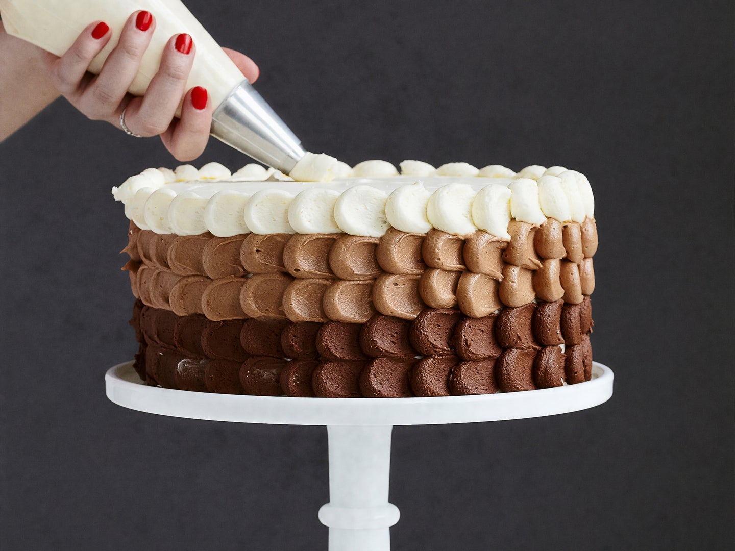 A person using a piping bag to pipe frosting onto a chocolate cake.