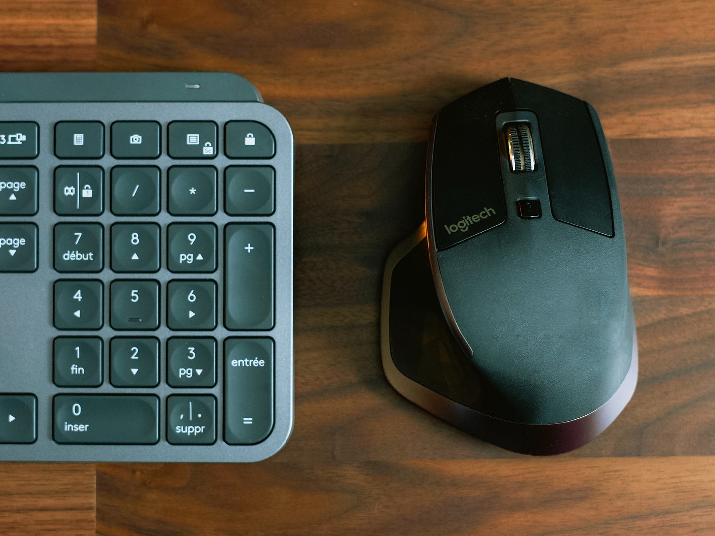 Black mouse and keyboard sitting side by side on a wooden desk.