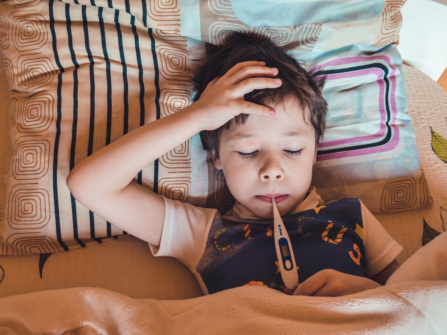 a kid sick in bed having his temperature taken