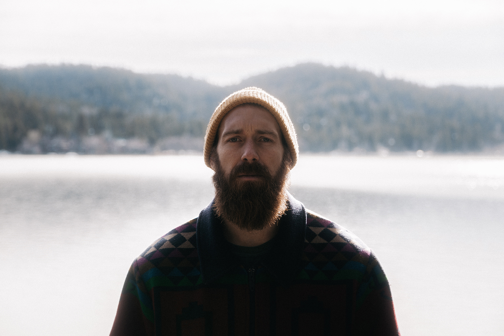 man standing in front of lake with a big beard and a beanie