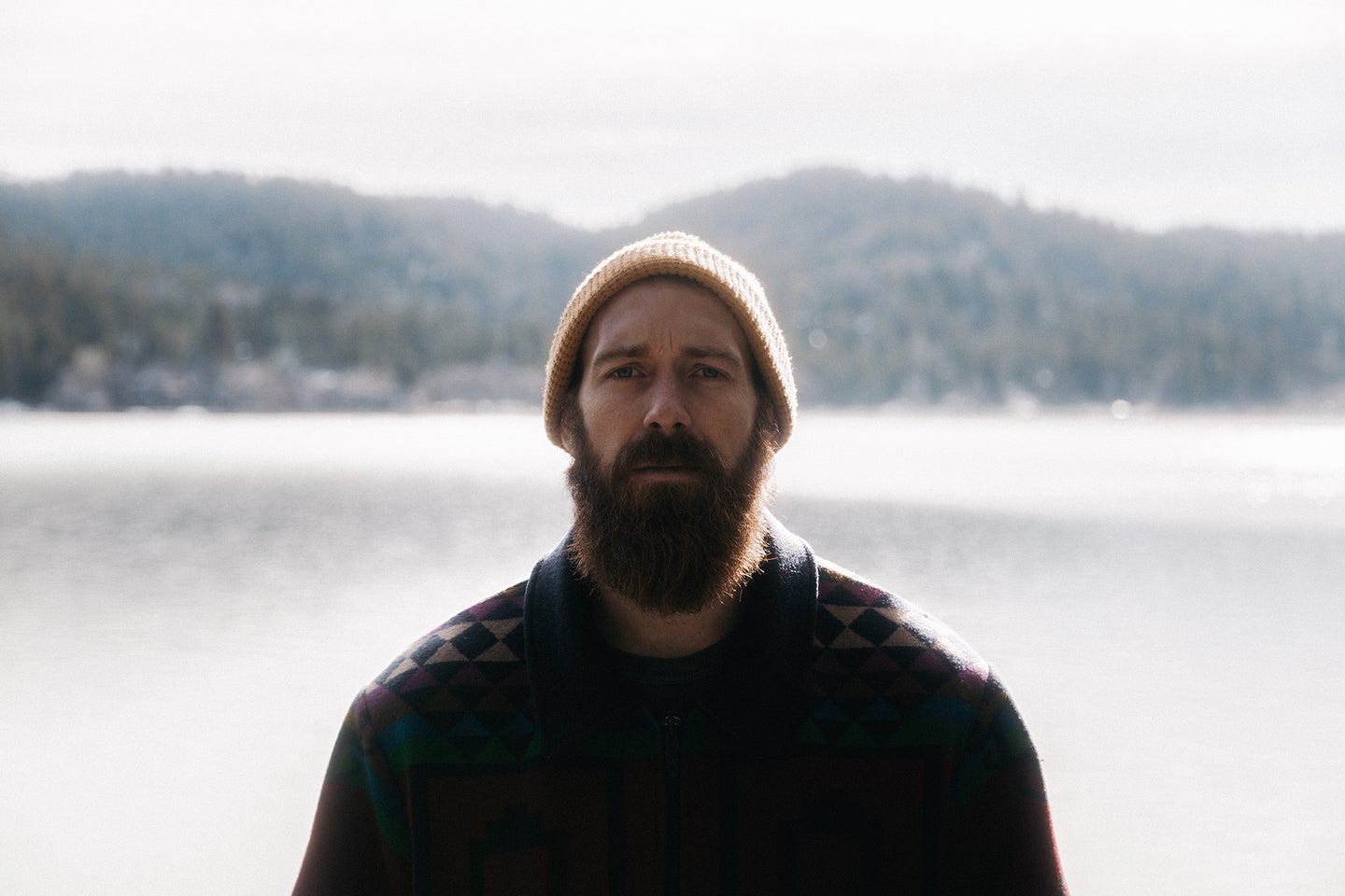 man standing in front of lake with a big beard and a beanie