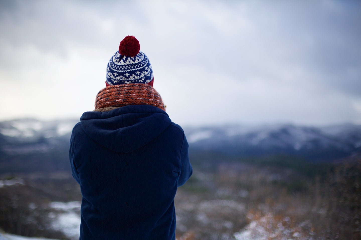 person with a winter hat and scarf looking out at a mountain