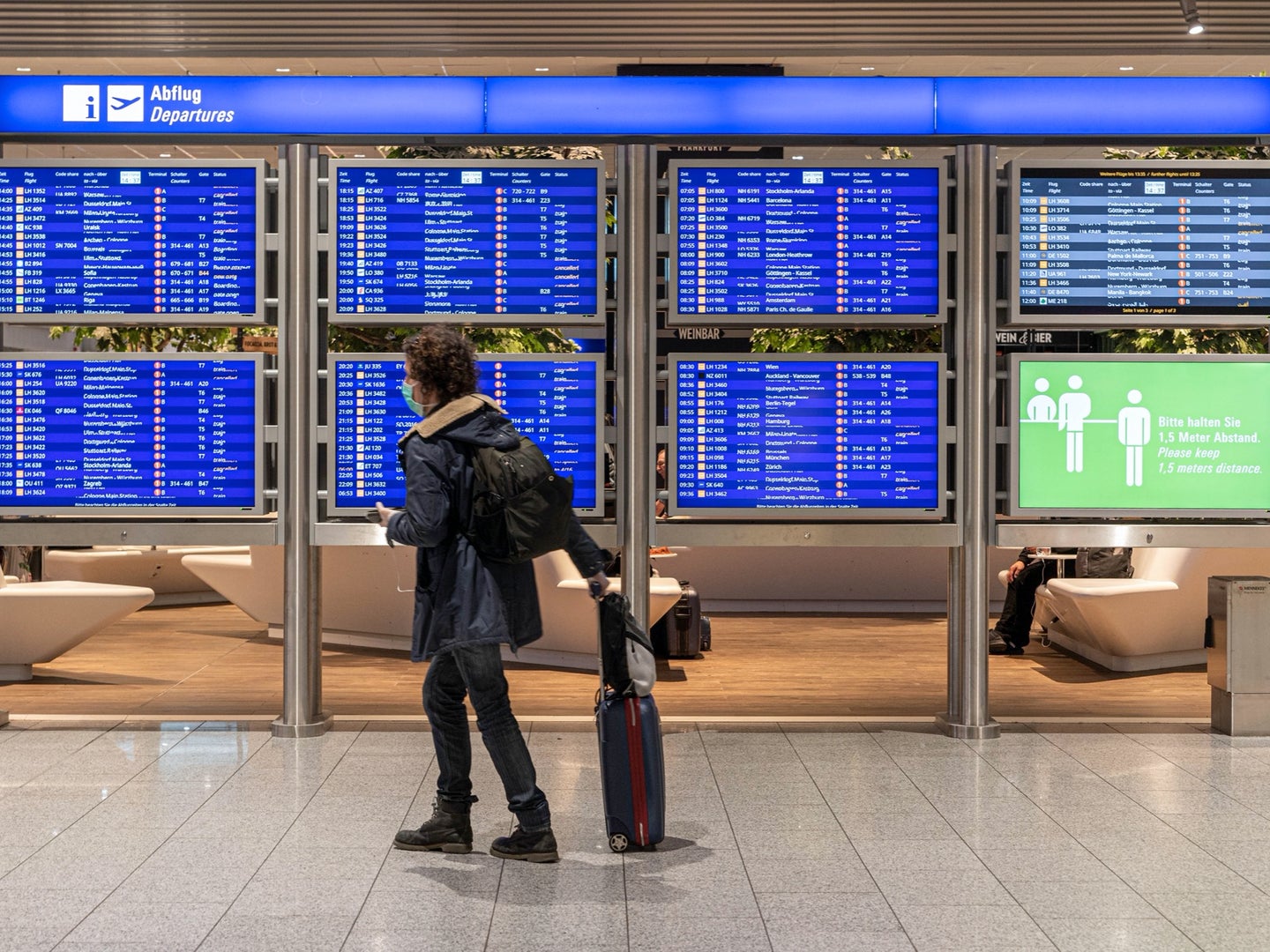 person wearing a mask and looking at the departures board at an airport