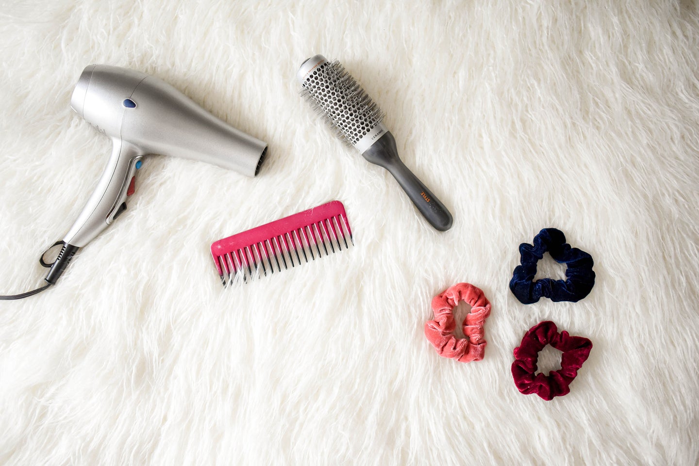 hair dryer, comb, brush, and scrunchies on a furry white rug