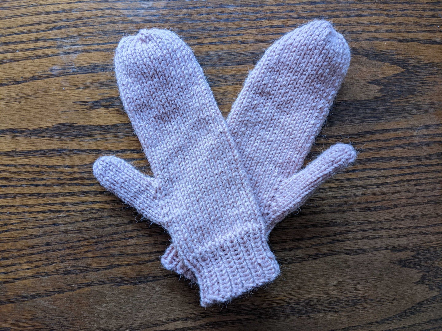 A pair of pink mittens on a wood surface.