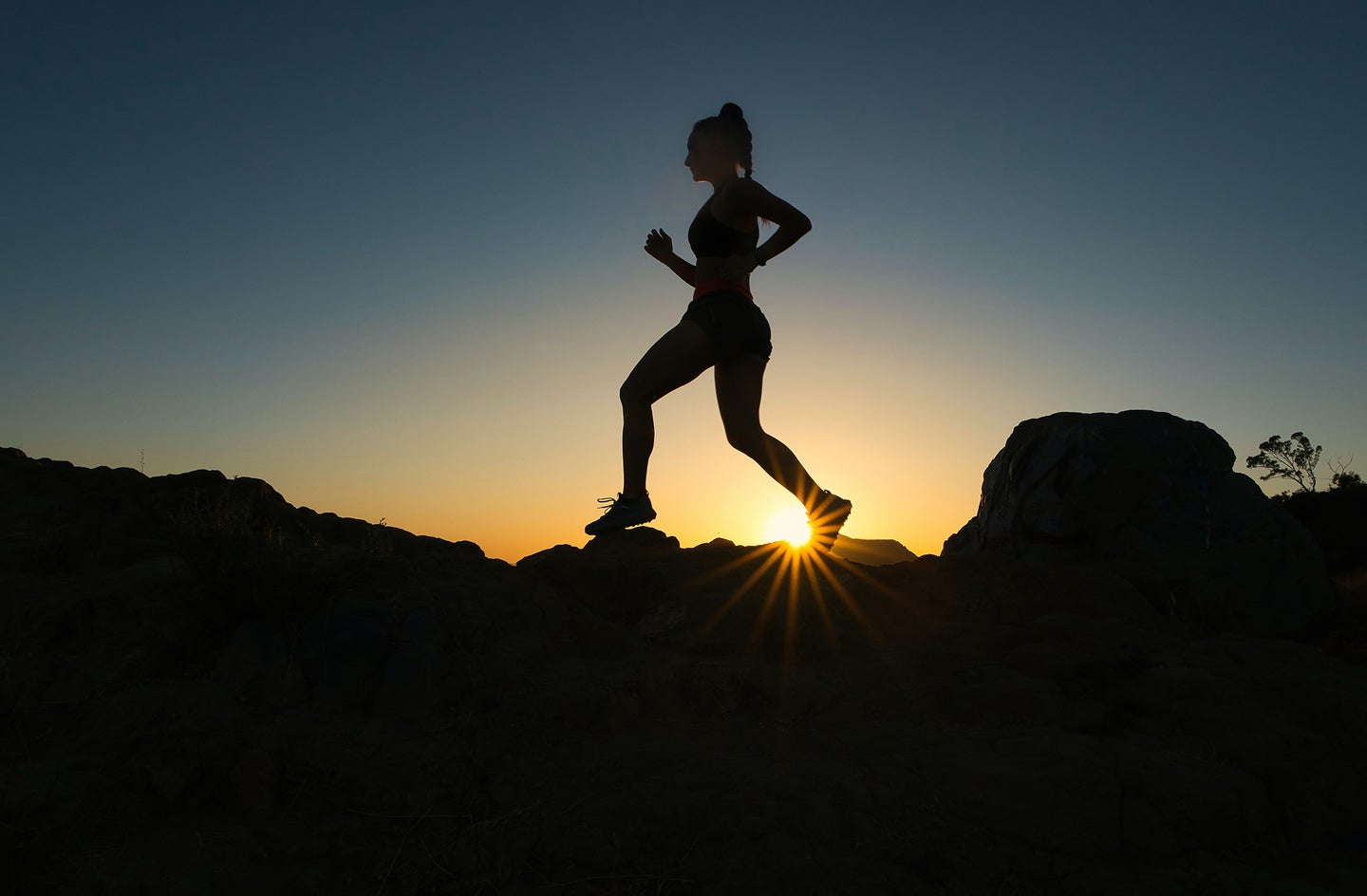 woman running on top of rocks with sun setting behind her
