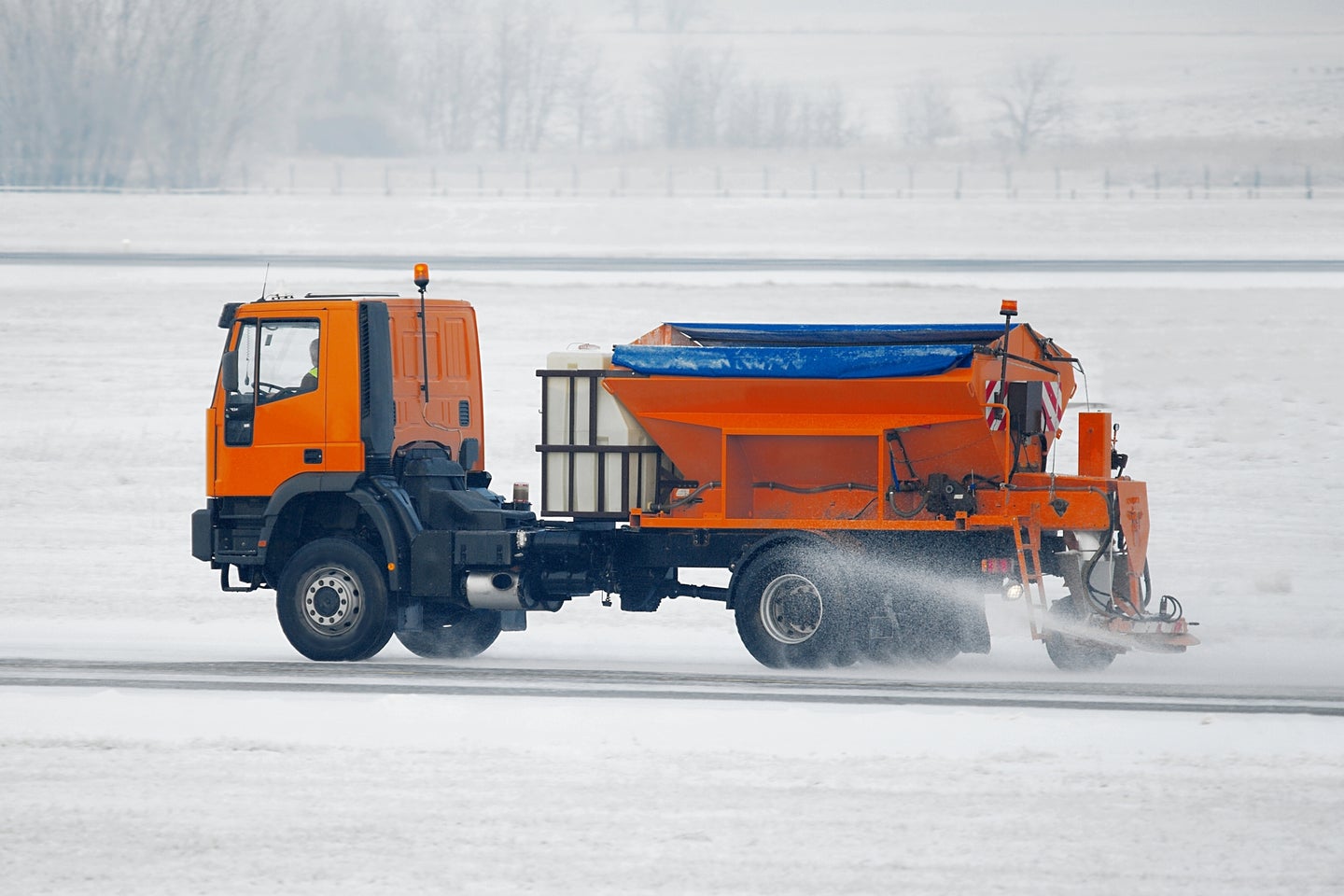 An orange truck spreading salt on a snowy airport runway
