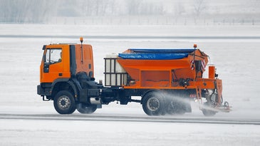An orange truck spreading salt on a snowy airport runway