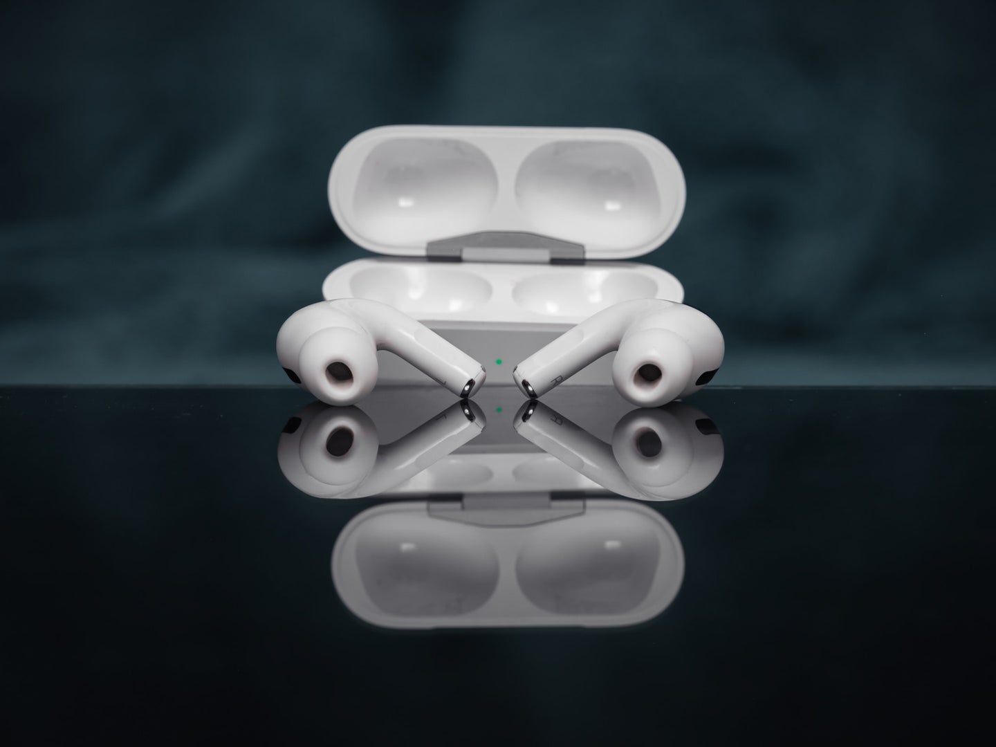 A pair of Apple's AirPods Pro on a reflective black surface, in front of their case.