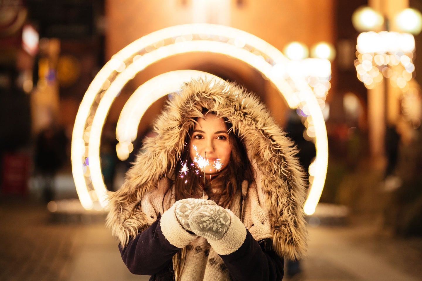 woman in a winter coat wearing the best mittens and holding sparklers