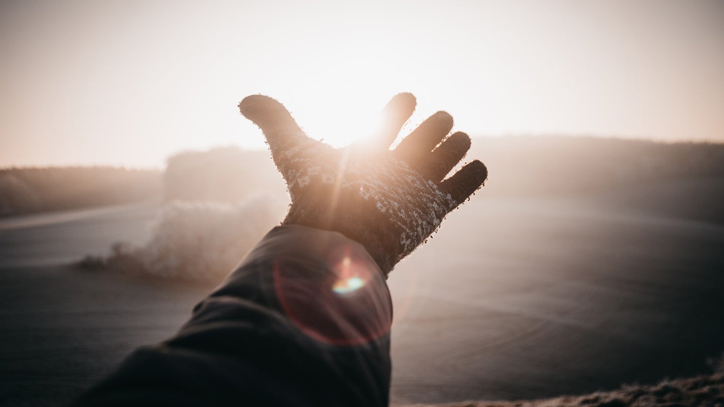 person with a glove reaching into the sky with the sun behind it