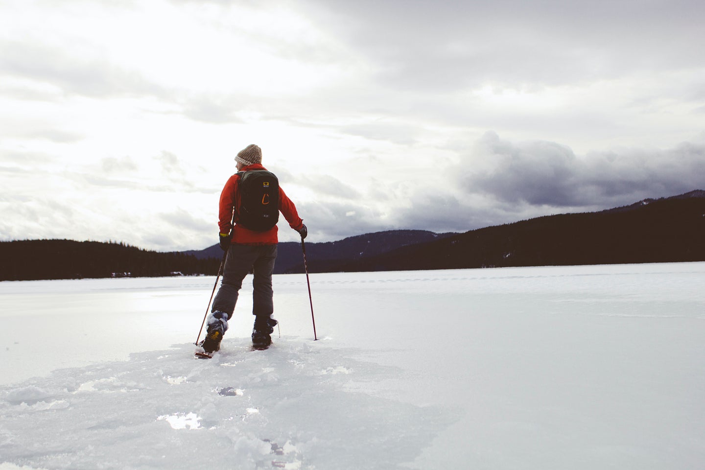 man wearing snowshoes with ski poles walking through snow