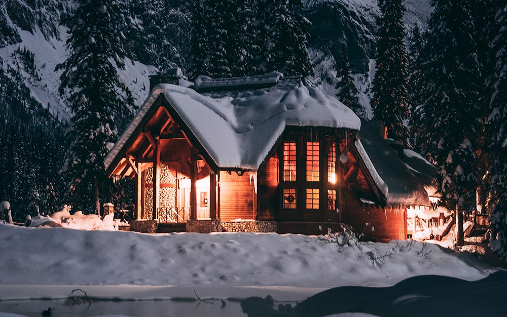 house with lights on covered in snow on a mountain