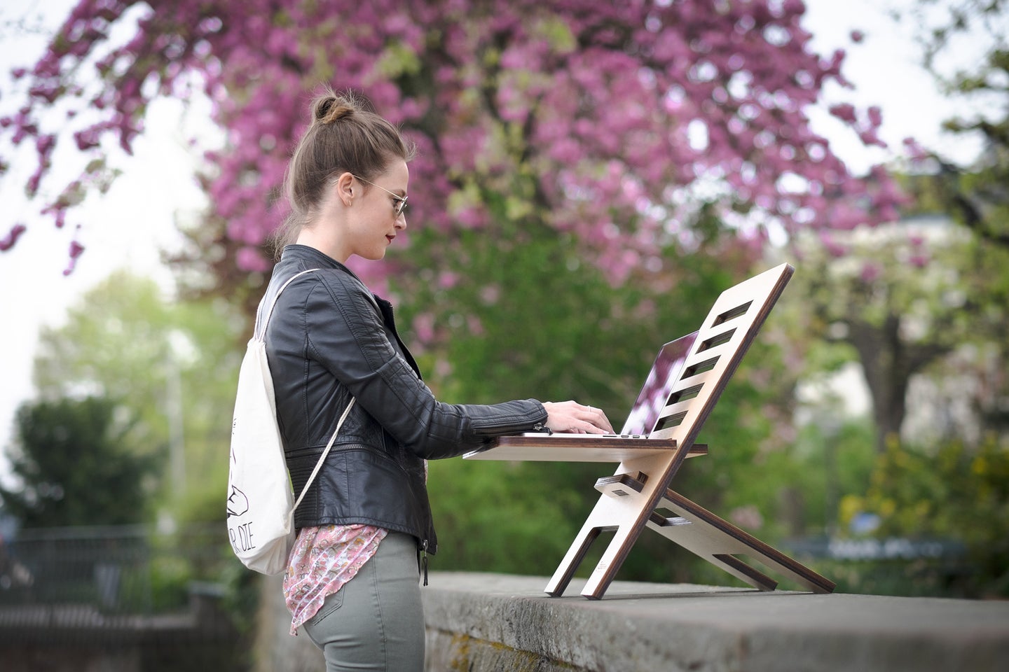 A woman outside, using the best portable wifi, with a white backpack working on a laptop placed on a folding laptop stand.