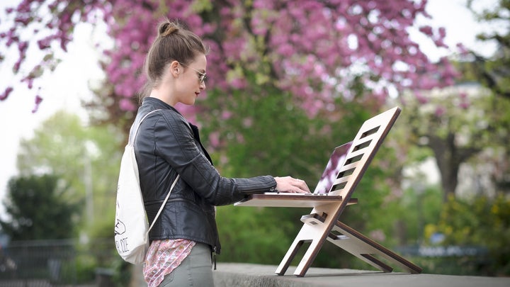A woman outside, using the best portable wifi, with a white backpack working on a laptop placed on a folding laptop stand.