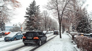 snowy street with tress, parked cars, and cars driving