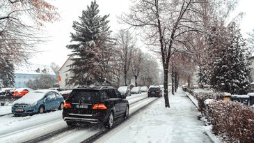 snowy street with tress, parked cars, and cars driving