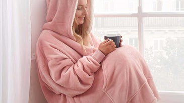 Woman holding cup of coffee wearing cozy and warm hoodie blanket.