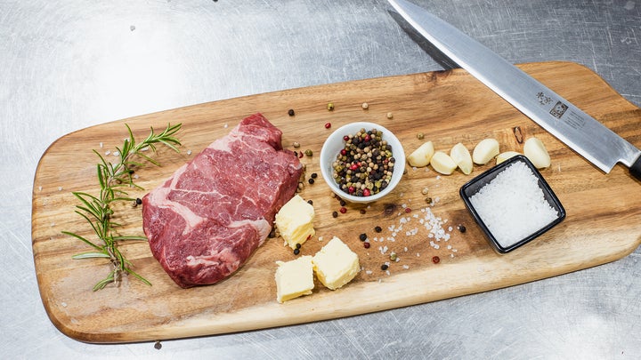 meat, cheese, pepper, and salt on a wood board next to a kitchen knife