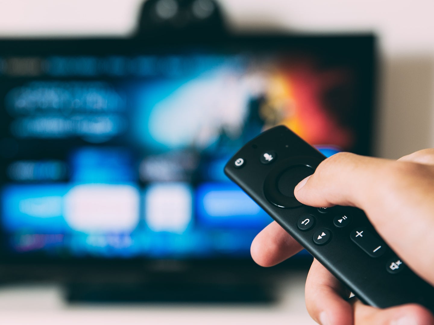 Hand holding Amazon Fire TV remote towards TV screen