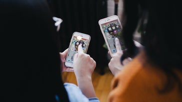 Two people facing away from the camera while pointing at their iPhones.