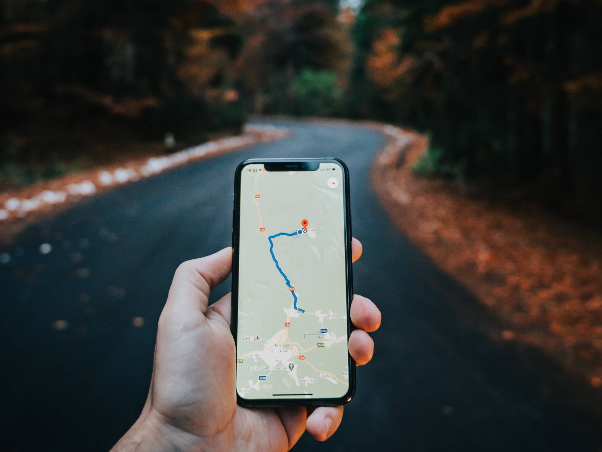 Hand holding a phone with a map in front of an empty road.