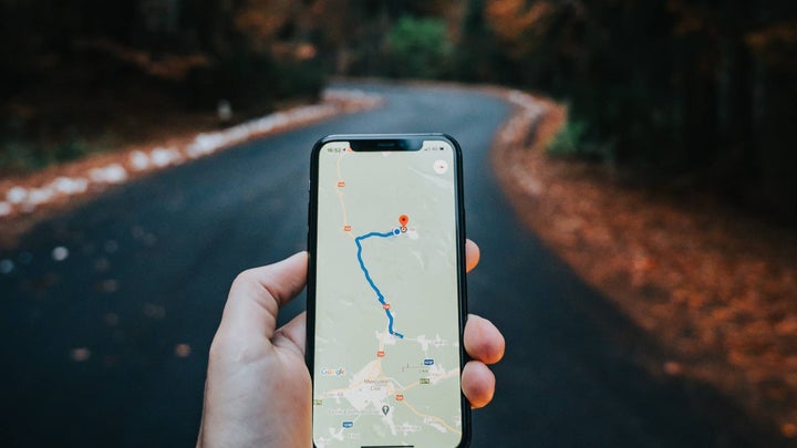 Hand holding a phone with a map in front of an empty road.