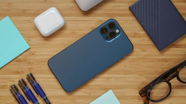 iphone 12 in one of the best iphone cases, glasses, pens, airpods, and hard drive on a wooden surface