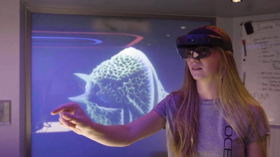A woman wearing a Microsoft Hololens and interacting with an invisible hologram that only she can see.