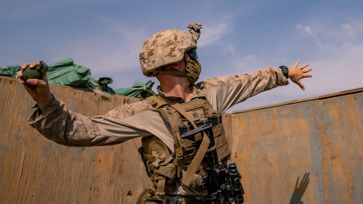 A US Marine in desert camo about to throw a grenade out of a bunker.