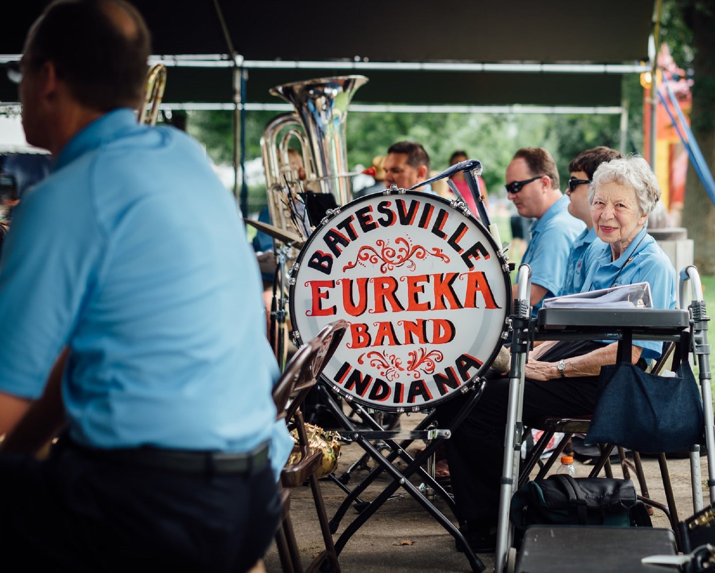Elderly person in a blue uniform sitting next to a marching band drum that says Batesville Eureka Band Indiana