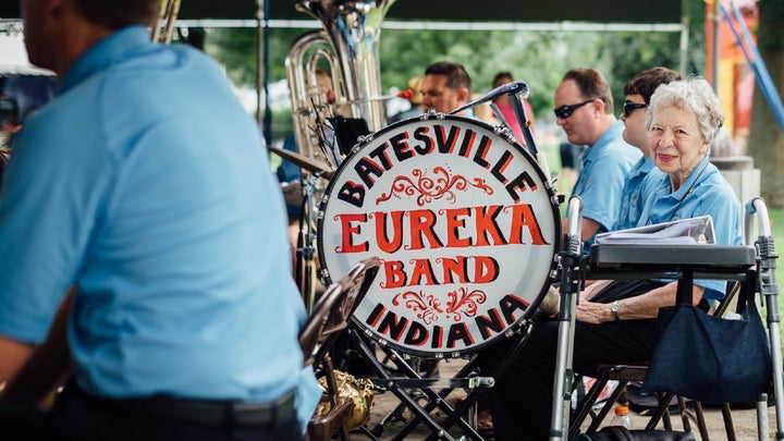 Elderly person in a blue uniform sitting next to a marching band drum that says Batesville Eureka Band Indiana