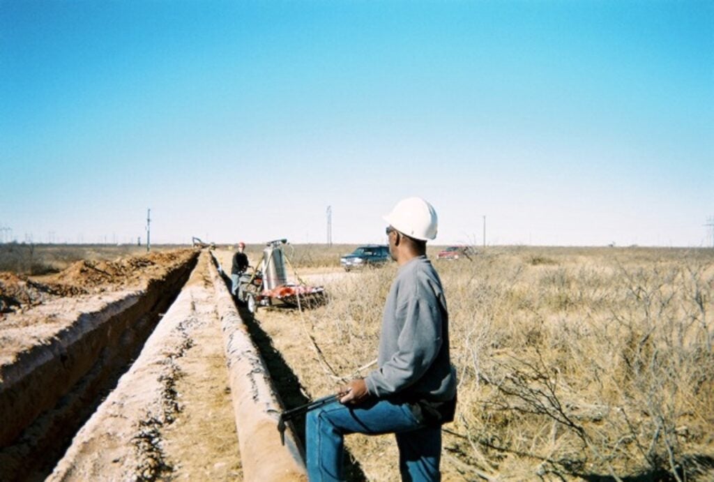 Gas pipeline worker in a white hard hat in tall grasses