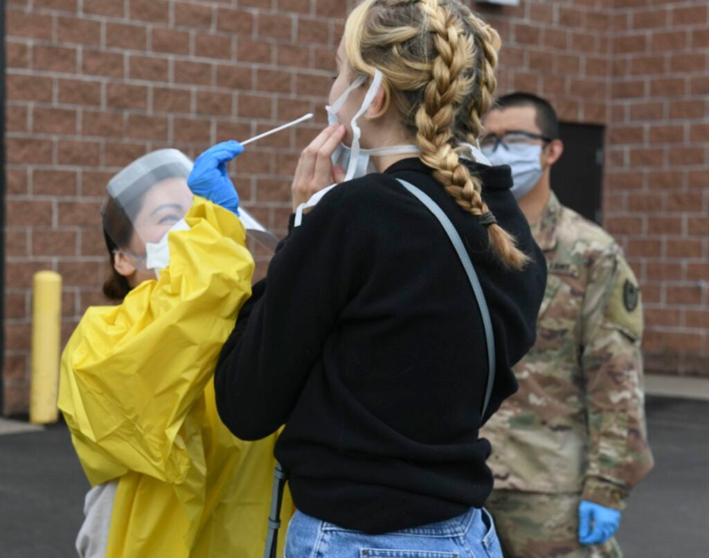 Nasal swab being used by a healthcare worker in PPE on a person with braids and a black hoodie